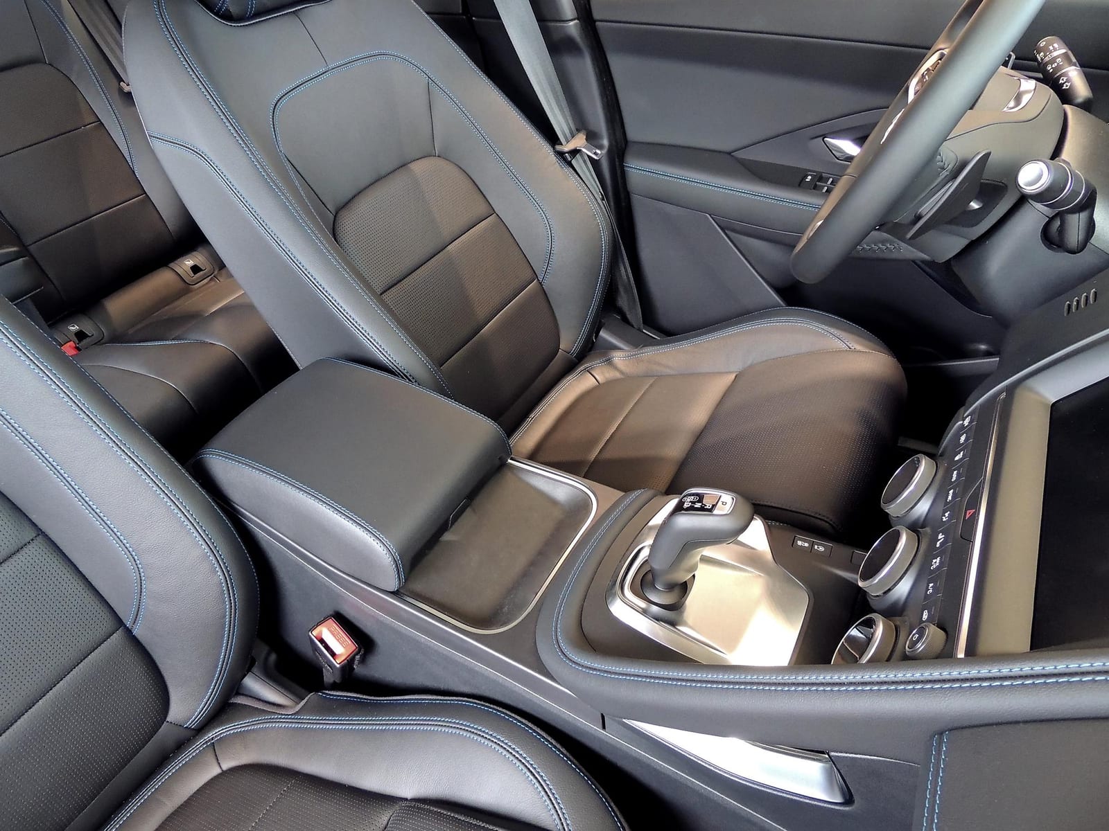 Bancos dianteiros em couro preto com costura azul no interior de um carro moderno.